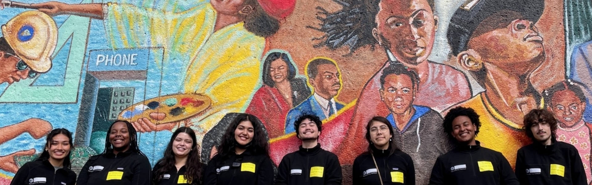 group of students standing near a wall mural. 